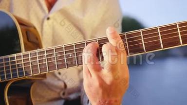 人手弹吉他对着湖面.. 吉他手触摸吉他弦。 近距离射击。